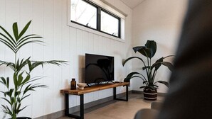 Een woonkamer met een televisie op een houten dressoir, een bankje en potplanten.