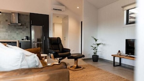 Een moderne woonkamer met een leren bank, een zwarte lederen fauteuil, een televisie, een klein tafeltje en een potplant.