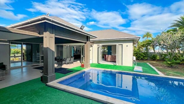 Una casa moderna con piscina, terraza cubierta y abundante vegetación.
