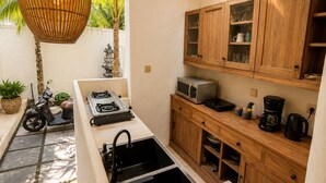 A compact kitchen with a gas stove, a microwave, and wooden cabinets. - EveEvy Private Pool Villas (Lembongan Island)