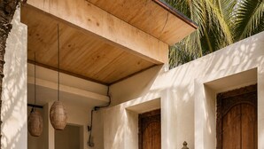 A courtyard with a wooden ceiling, two doors with intricate carvings, a small statue, a potted plant, and hanging wicker lamps. - EveEvy Private Pool Villas (Lembongan Island)