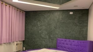 Pyöreä, violetti sänky, jossa on napitettu pääty, vihreä, kuvioitu seinä ja kattovalaisin.