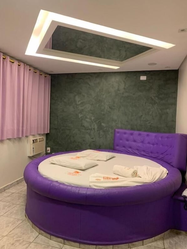 A circular purple bed with a tufted headboard, a green textured wall, and a ceiling light fixture. - Caribe Palace Hotel Samambaia Sul (Samambaia)
