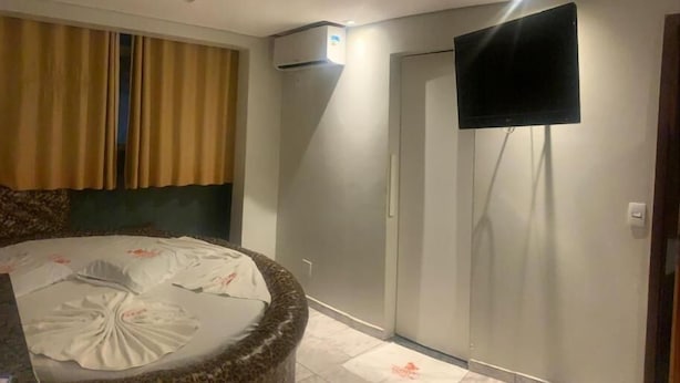Hotellihuone, jossa on sänky, seinälle asennettu televisio ja ilmastointilaite.