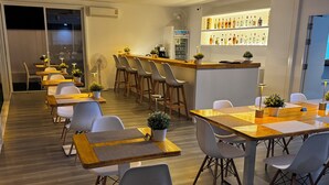 Um restaurante moderno com mesas e cadeiras de madeira, área de bar com diversos tipos de garrafas e uma geladeira.
