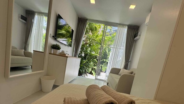 Quarto de hotel moderno com uma cama, um sofá, uma televisão e vista para o verde lá fora.