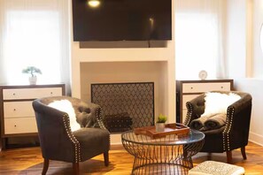 A living room with a fireplace, two armchairs, a coffee table, and a TV mounted on the wall. - Spacious 4-bedroom apartment in fantastic Chicago with AC (Chicago)