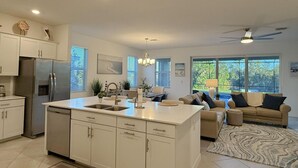 A modern kitchen with a central island, white cabinetry, and a dining area with a sofa and a view of the outdoors.