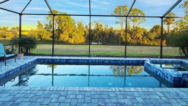 A swimming pool with a glass enclosure, surrounded by a paved deck and a covered seating area.