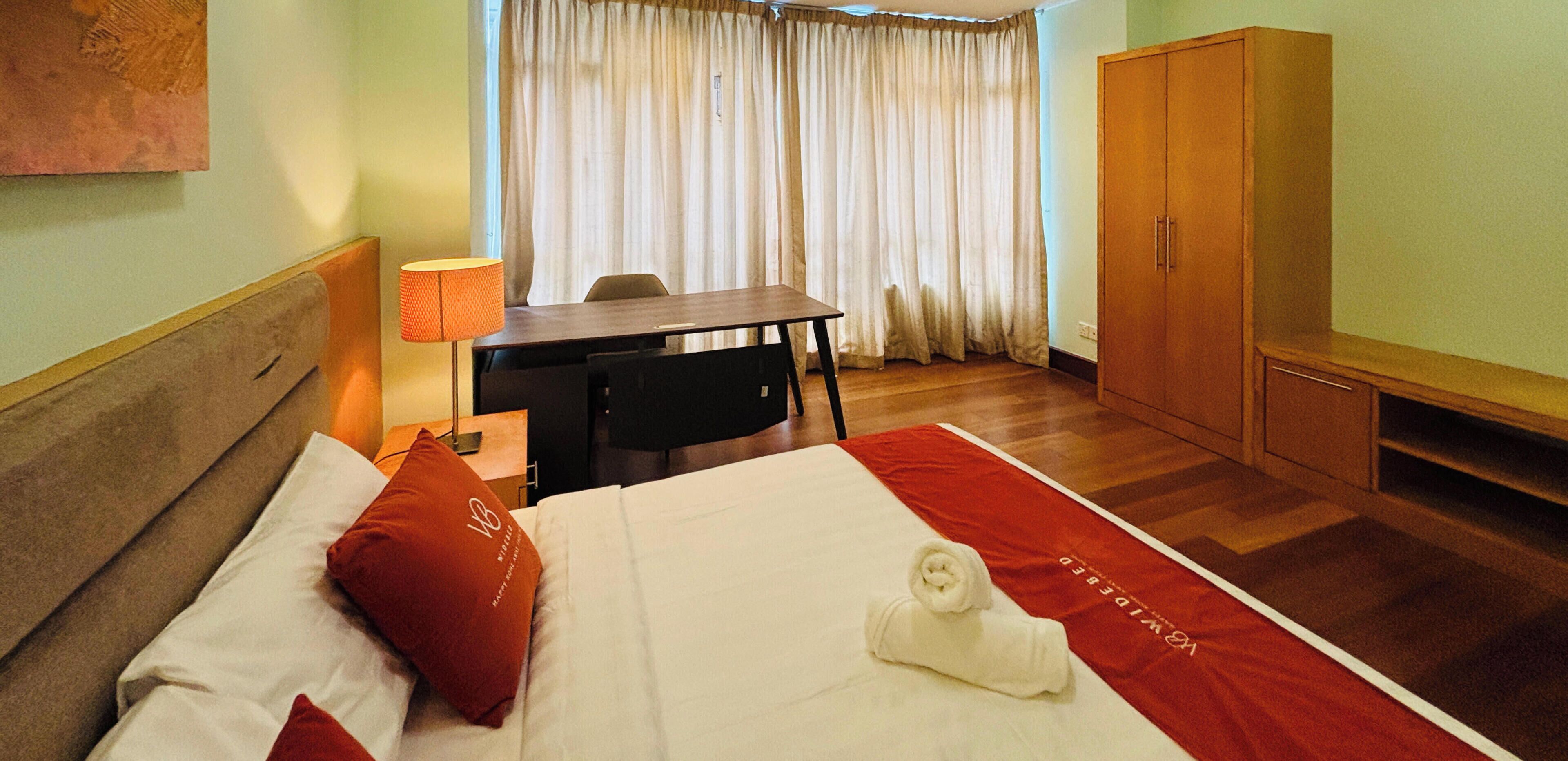 A hotel room with a bed, a desk, a chair, a wardrobe, and a window with curtains.