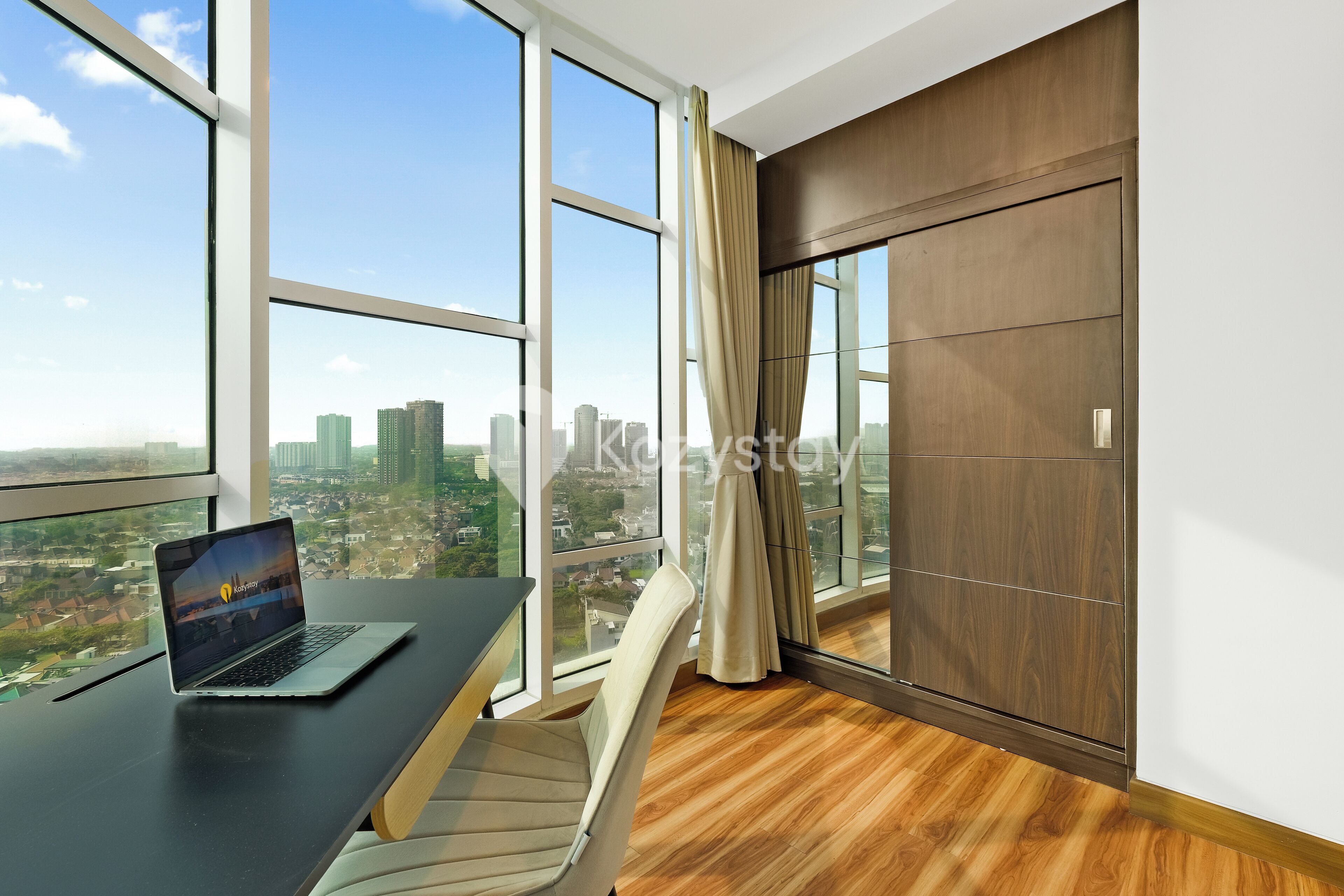 A modern office space with a large desk, laptop, and a view of a cityscape through large windows.