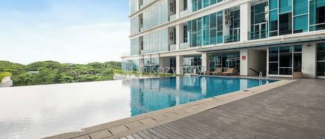 A modern hotel with a rooftop infinity pool, a wooden deck, and a view of lush greenery.