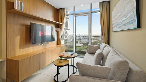 Ein modernes Wohnzimmer mit einem großen Flachbildfernseher, einer Couch, einem kleinen Tisch mit einer Pflanze und einem großen Fenster mit Blick auf die Stadt.