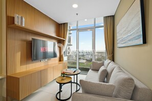 Un soggiorno moderno con una grande TV a schermo piatto, un divano, un tavolino con una pianta e un'ampia finestra che offre vista sulla città.