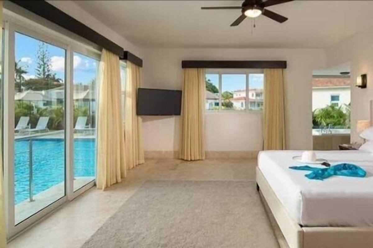 Ein Hotelzimmer mit einem großen Bett, einem Deckenventilator, einem Fernseher und Blick auf einen Swimmingpool.