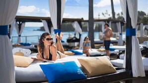 Een hotelkamer aan het strand met een bed, kussens en uitzicht op zee.