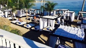 Een strandresort met meerdere ligbedden en cabana's, met uitzicht op de oceaan.