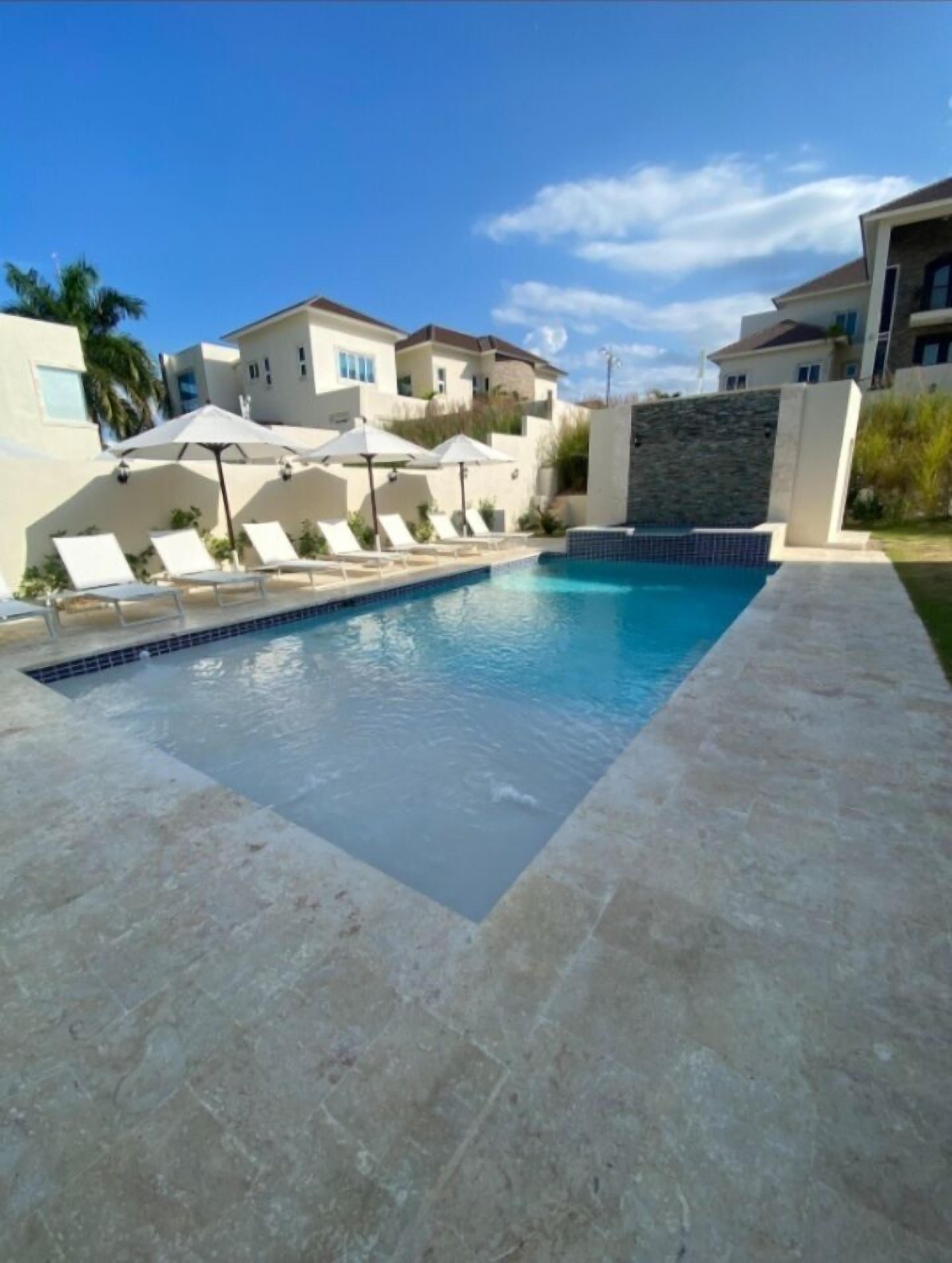 Una piscina con sillas de descanso y sombrillas, rodeada de casas.