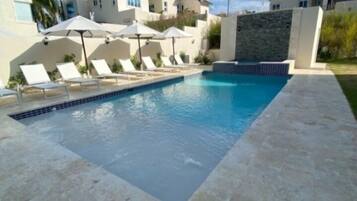 Una piscina con sillas de descanso y sombrillas, rodeada de casas.