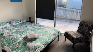 A bedroom with a bed, a chair, a painting, and a view of the outside. - Dog friendly Northland getaway - Hihi Beach (Hihi)