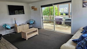 A modern living room with a sofa, a wooden coffee table, and a TV mounted on the wall. - Dog friendly Northland getaway - Hihi Beach (Hihi)