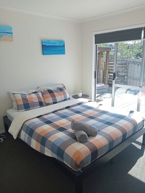 A bedroom with a bed, a painting, and a view through a sliding door.