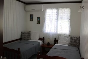 A room with two single beds, a small table, a lamp, and an air conditioning unit. - Apartments Pepe's View - B (Aguada)