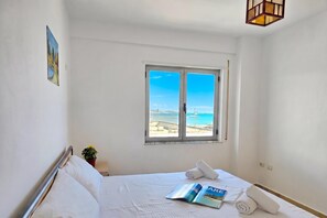 Une chambre d’hôtel avec un lit, une fenêtre donnant sur la mer, une petite table avec une plante et un magazine posé sur le lit.