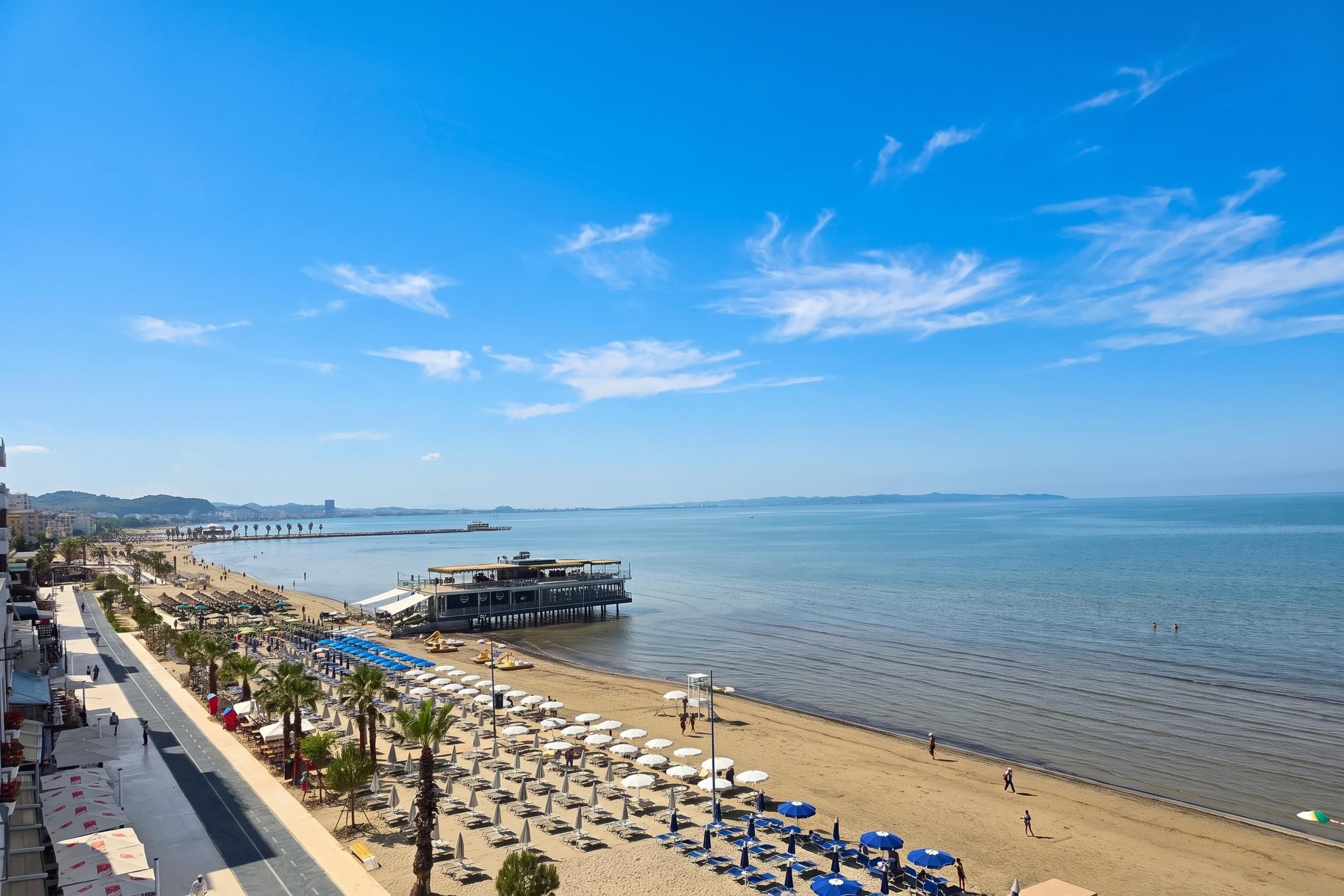 Vista costera con playa, sombrillas y un muelle.