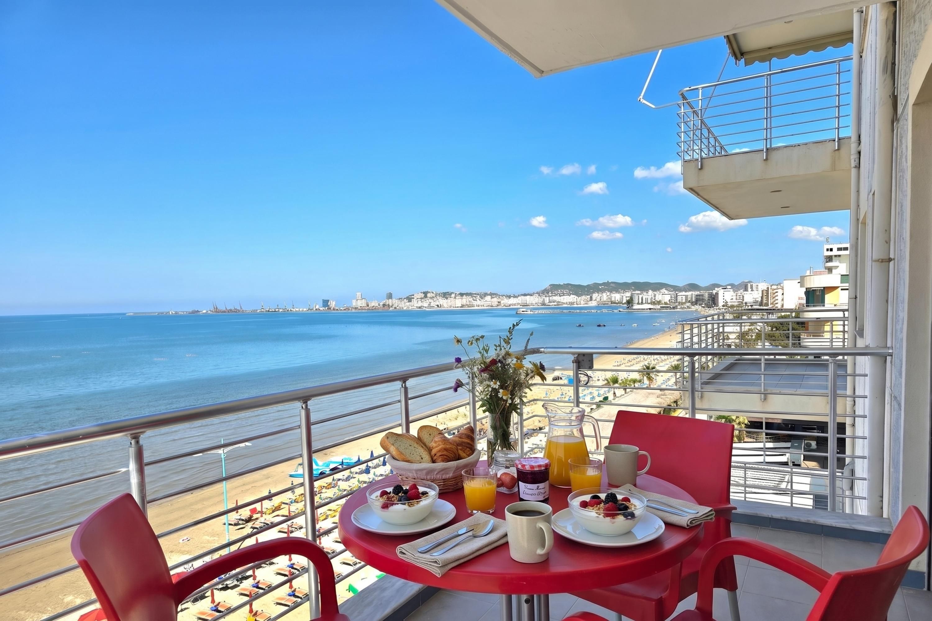 A balcony table with breakfast items, overlooking a beach and cityscape.