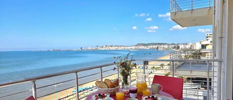 A balcony table with breakfast items, overlooking a beach and cityscape.