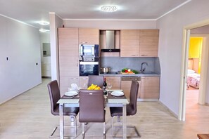 A modern kitchen with built-in appliances, a dining area with a table set for two, and a view into a bedroom. - Sea Vista Durres 50m from beach, Durres, Albania (Durres)