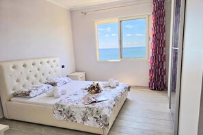 A bedroom with a large bed, a nightstand, a window with a view of the sea, and a curtain. - Sea Vista Durres 50m from beach, Durres, Albania (Durres)