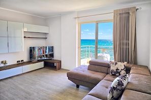 A modern living room with a sofa, a flat-screen TV, a bookshelf, and a large window with a view of the sea. - Sea Vista Durres 50m from beach, Durres, Albania (Durres)