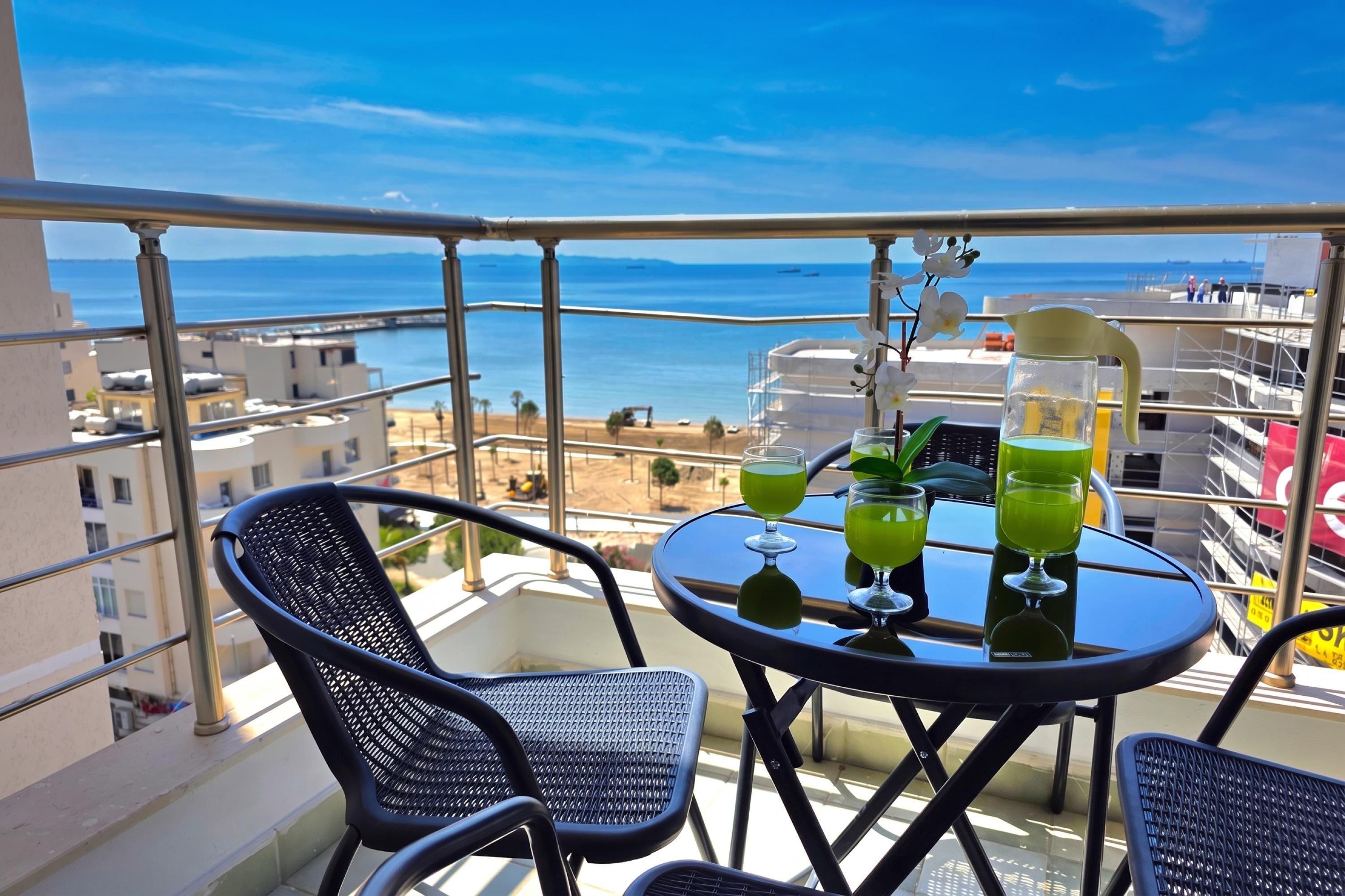 A balcony with a table set for two, overlooking a coastal view.