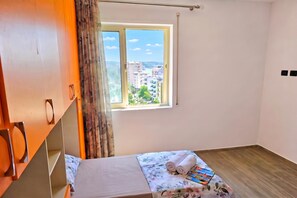 A small, bright room with a bed, a window with a view of buildings, and a wardrobe. - Sea Vista Durres 50m from beach, Durres, Albania (Durres)