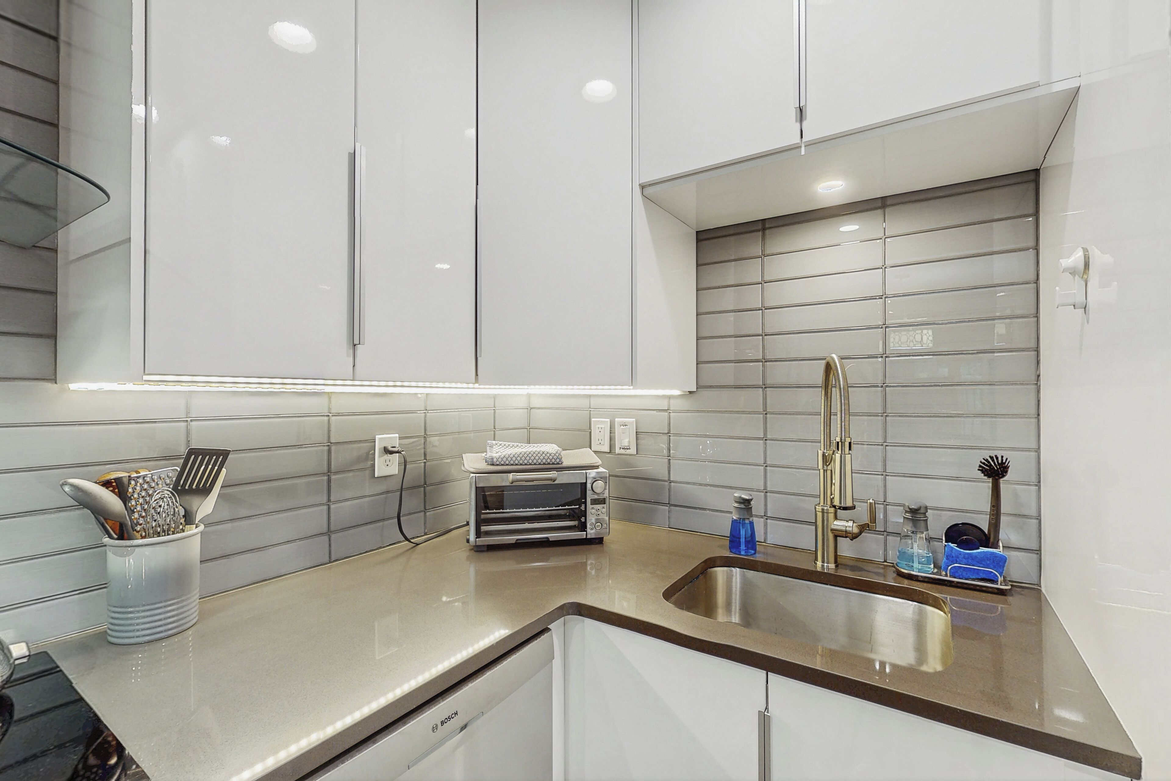 Una cocina moderna con armarios blancos, un lavamanos de acero inoxidable y un lavavajillas Bosch.