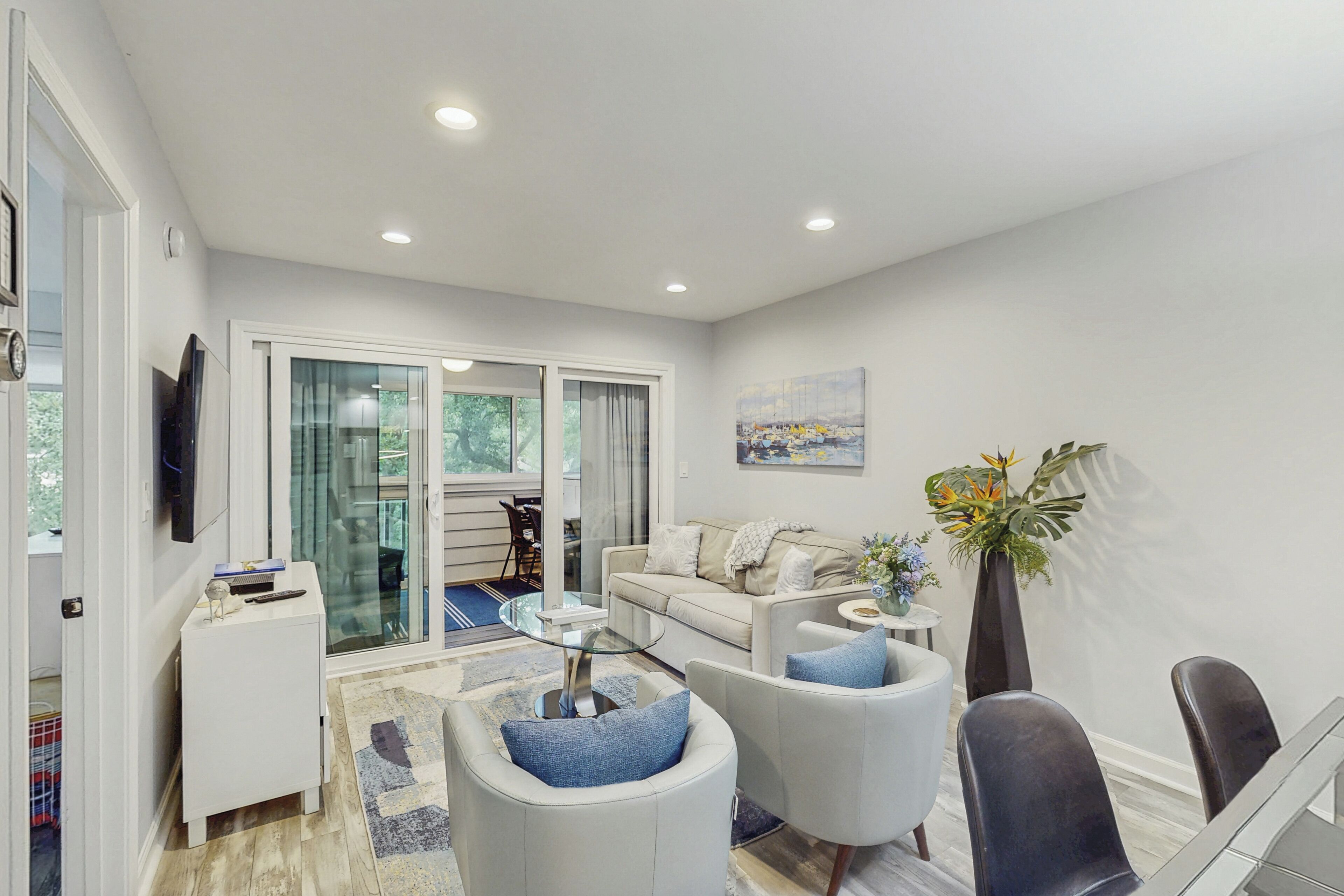 A modern living room with a sofa, armchairs, a glass coffee table, and a dining area with chairs and a table.