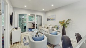 A modern living room with a sofa, armchairs, a glass coffee table, and a dining area with chairs and a table. - Hilton Head Haven: Beach House Lookout w/ Pool (Hilton Head Island)