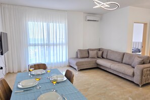 Un salon moderne comprenant un coin repas, un canapé et un téléviseur fixé au mur.