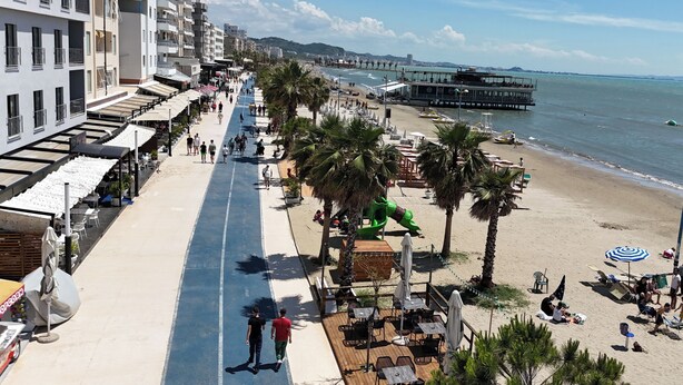 Eine Küstenpromenade mit Strand, Palmen und einem Steg.