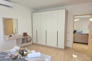 A modern bedroom with a large wardrobe, a bedside table with a magazine and flowers, and a bathroom visible through an open door. - Sea View Apartment in Durres Beach 100, Durres, Albania (Durres)