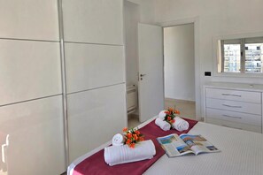 Habitación de hotel con una cama, ventana con vista a edificios, una puerta y un armario blanco.
