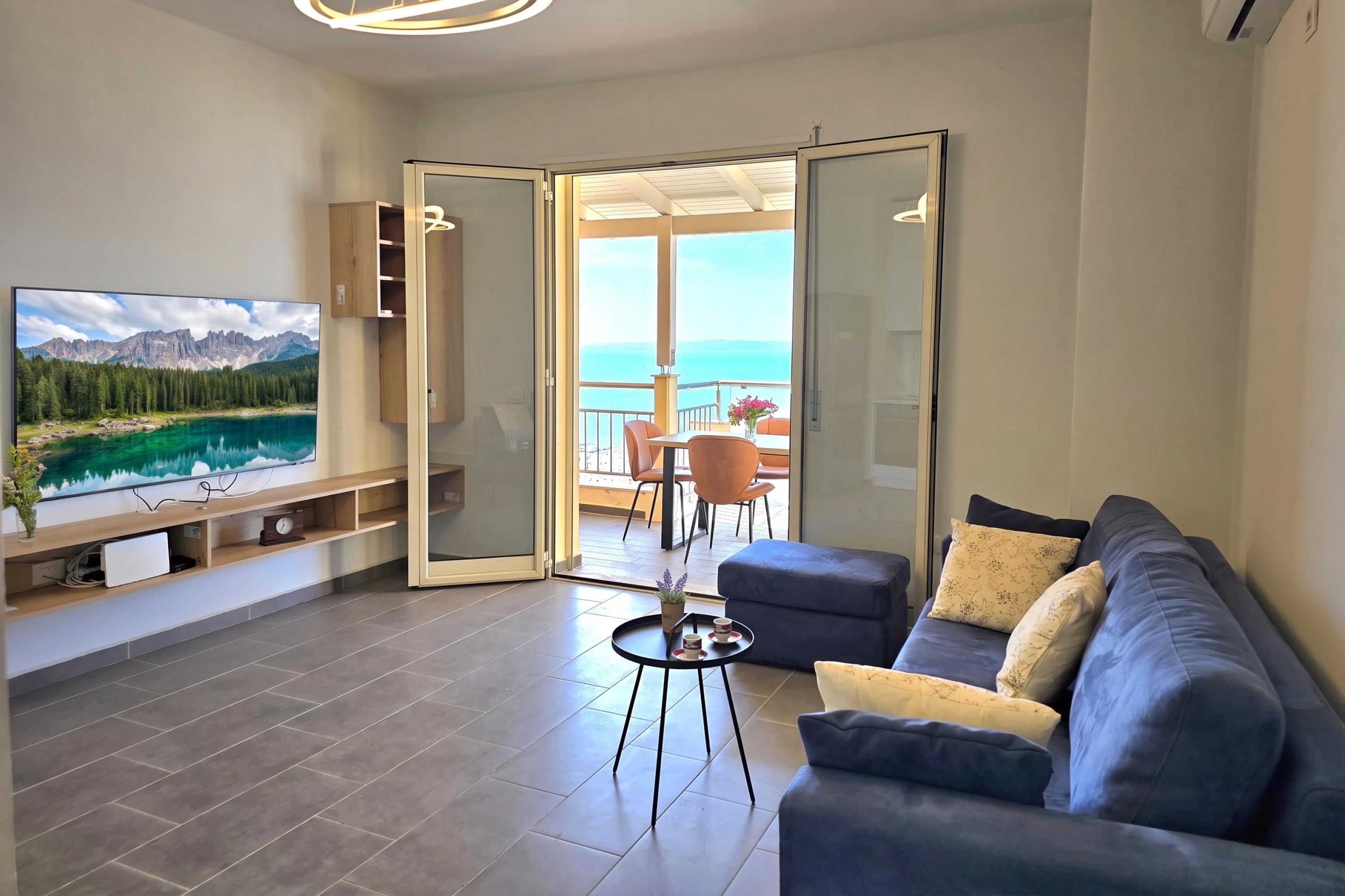 Un salón moderno con televisor de pantalla plana, un sofá y un balcón con vistas al mar.