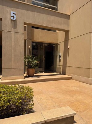 A modern building entrance with a number '5' sign, a potted plant, and a small bench.