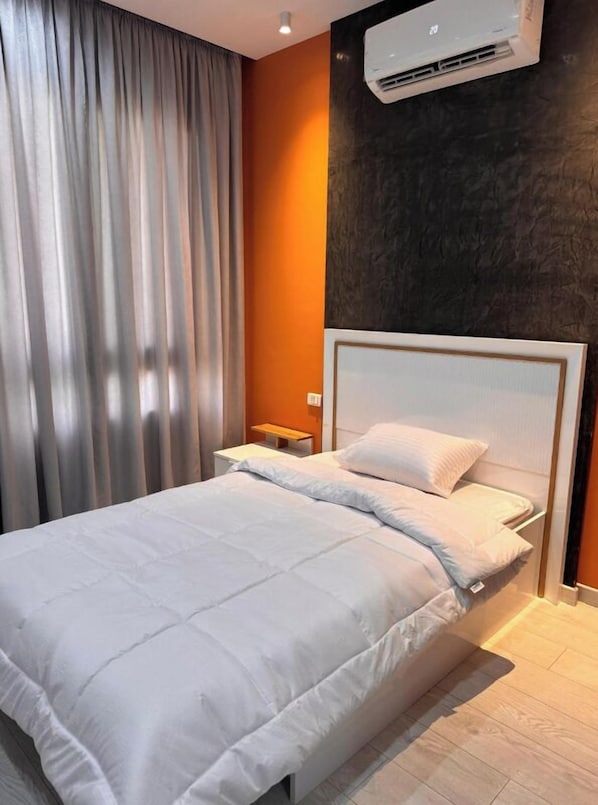 A modern hotel room with a large bed, a nightstand, an air conditioning unit, and a view of the city.
