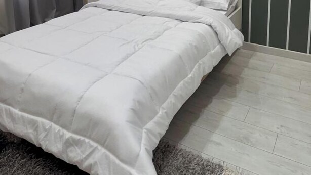 A bedroom with a bed, white bedding, a grey striped wall, and an air conditioning unit.