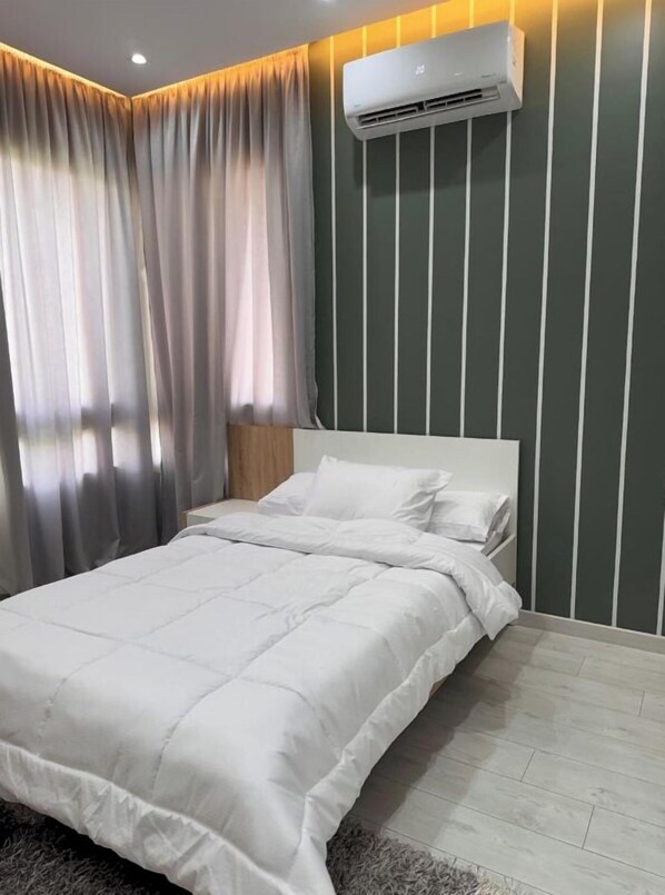 A bedroom with a bed, white bedding, a grey striped wall, and an air conditioning unit.