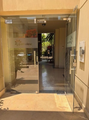 A modern building entrance with a glass door, a sign reading "parkview," and a visible outdoor area with a bench and greenery.