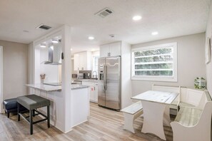 Een moderne keuken met witte kasten, een roestvrijstalen koelkast en een eethoek met een witte tafel en bank.